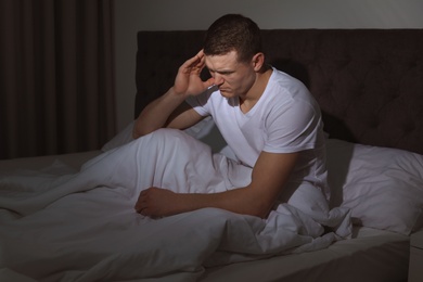 Handsome young man suffering from headache while sitting in bed at night