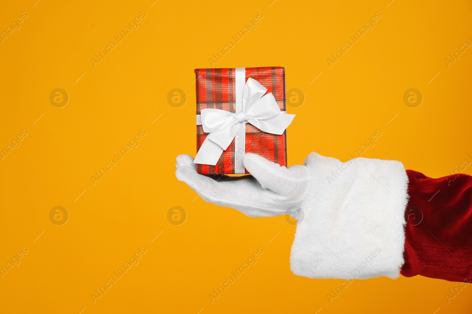 Photo of Santa Claus holding Christmas gift on yellow background, closeup of hand