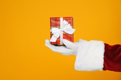 Photo of Santa Claus holding Christmas gift on yellow background, closeup of hand