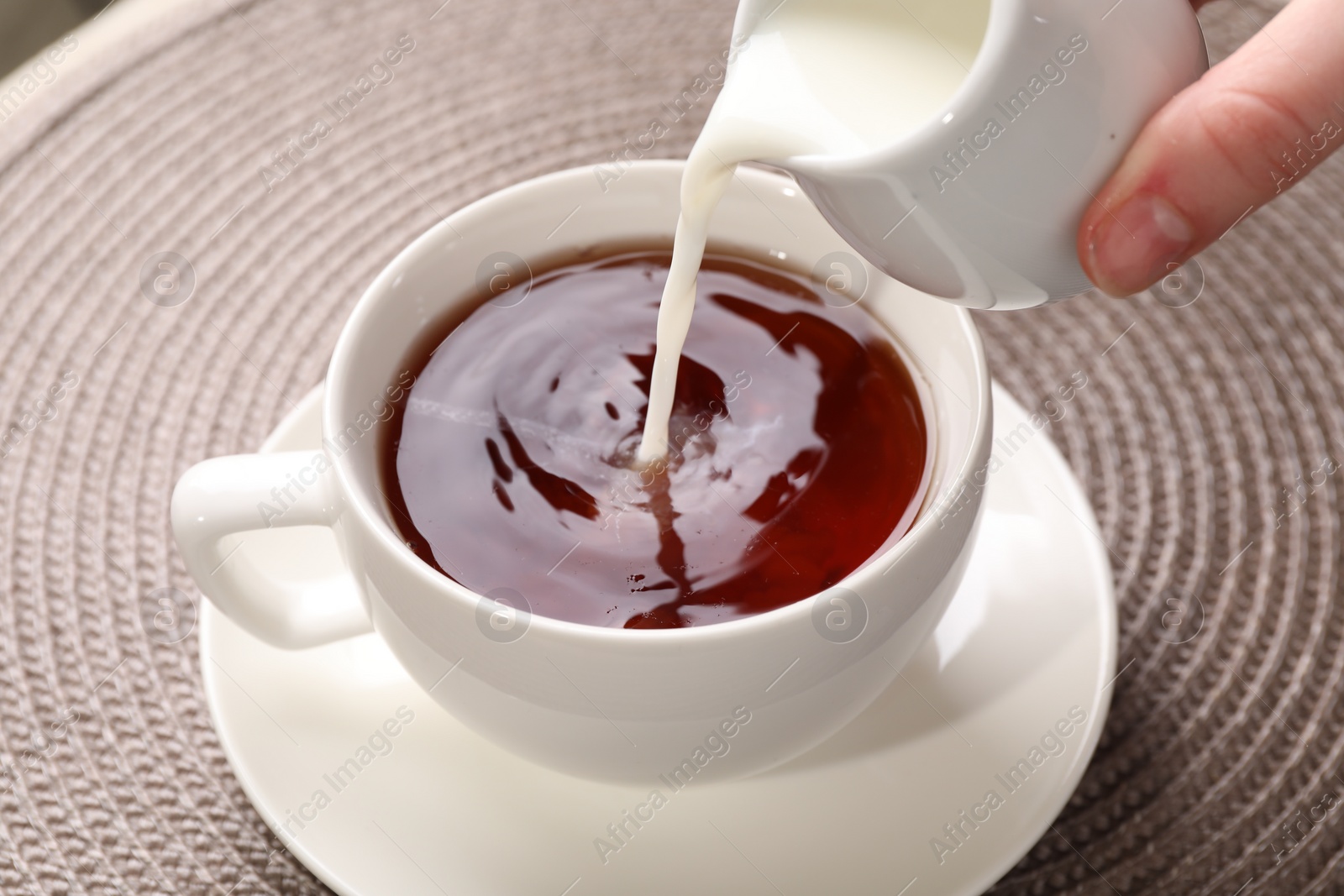 Photo of Woman pouring milk into cup with aromatic tea at table, closeup