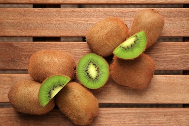 Whole and cut kiwis on wooden table, flat lay