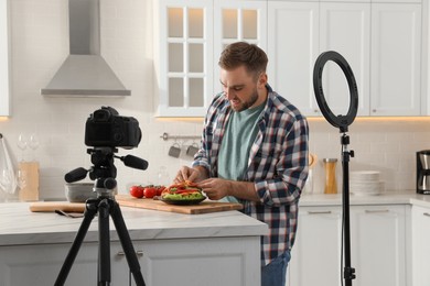 Photo of Blogger with tasty croissant recording video in kitchen at home. Using ring lamp and camera
