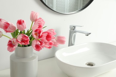 Vase with beautiful pink tulips near sink in bathroom