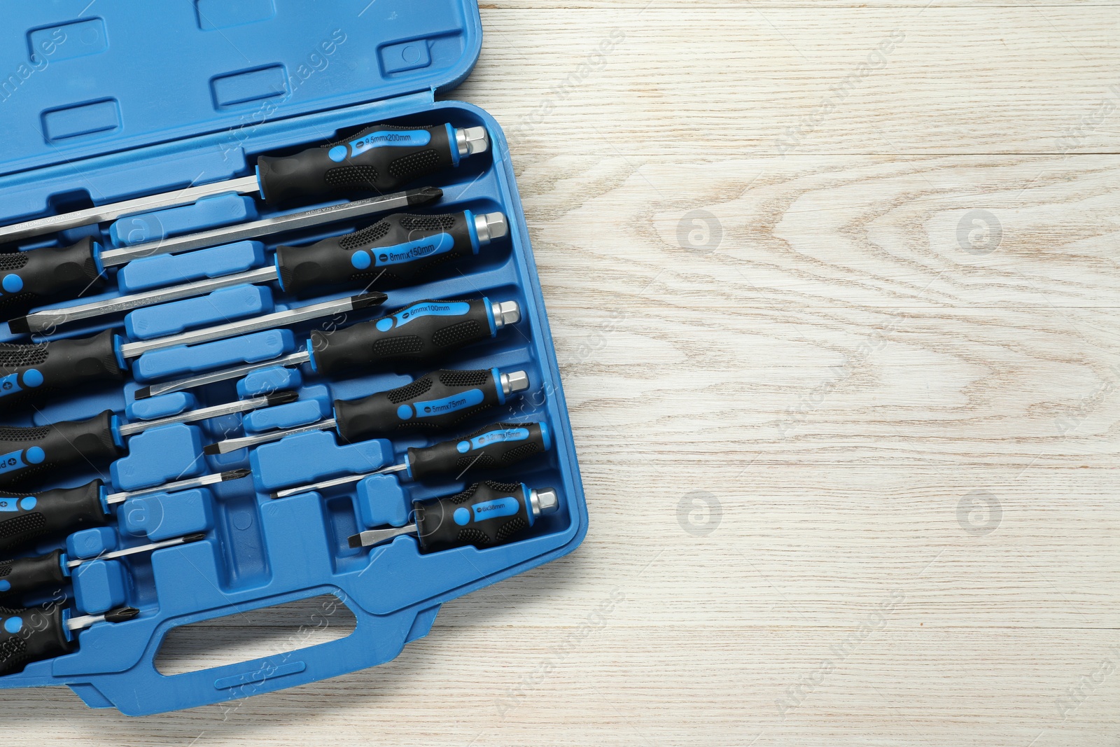 Photo of Set of screwdrivers in open toolbox on light wooden table, top view. Space for text