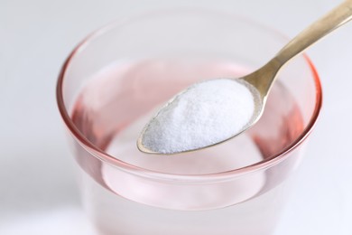 Photo of Spoon with baking soda over glass of water on white background, closeup