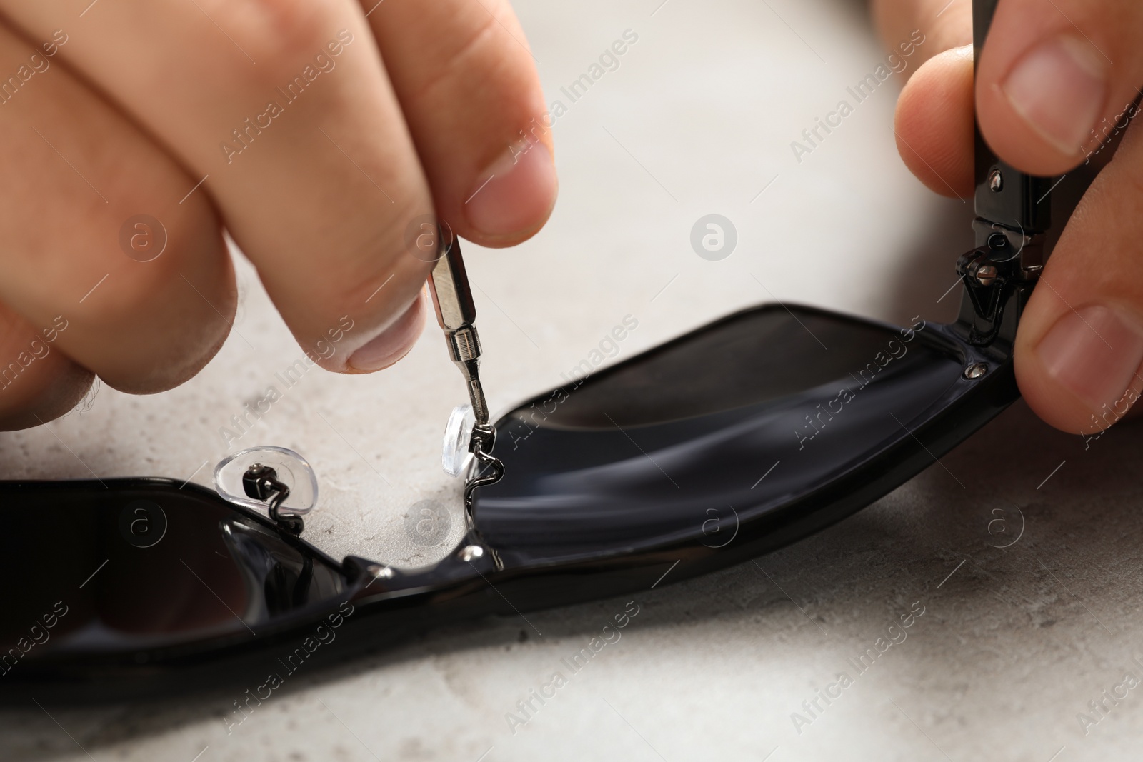 Photo of Handyman repairing sunglasses with screwdriver at grey table, closeup