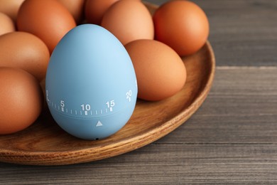 Plate with kitchen timer and chicken eggs on wooden table, closeup