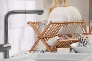 Photo of Sink and drying rack with clean dishes and cutlery on countertop in kitchen