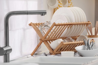 Sink and drying rack with clean dishes and cutlery on countertop in kitchen