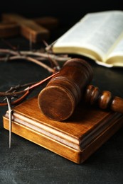 Photo of Wooden judge gavel and crown of thorns on black table, closeup