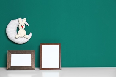 Photo of Soft toys and photo frames on table against green background, space for text. Child room interior