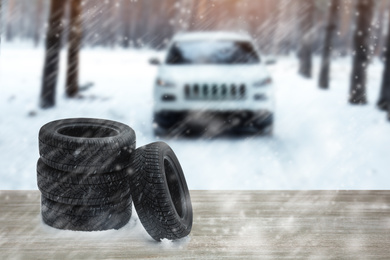Snow tires on wooden surface and winter landscape with car