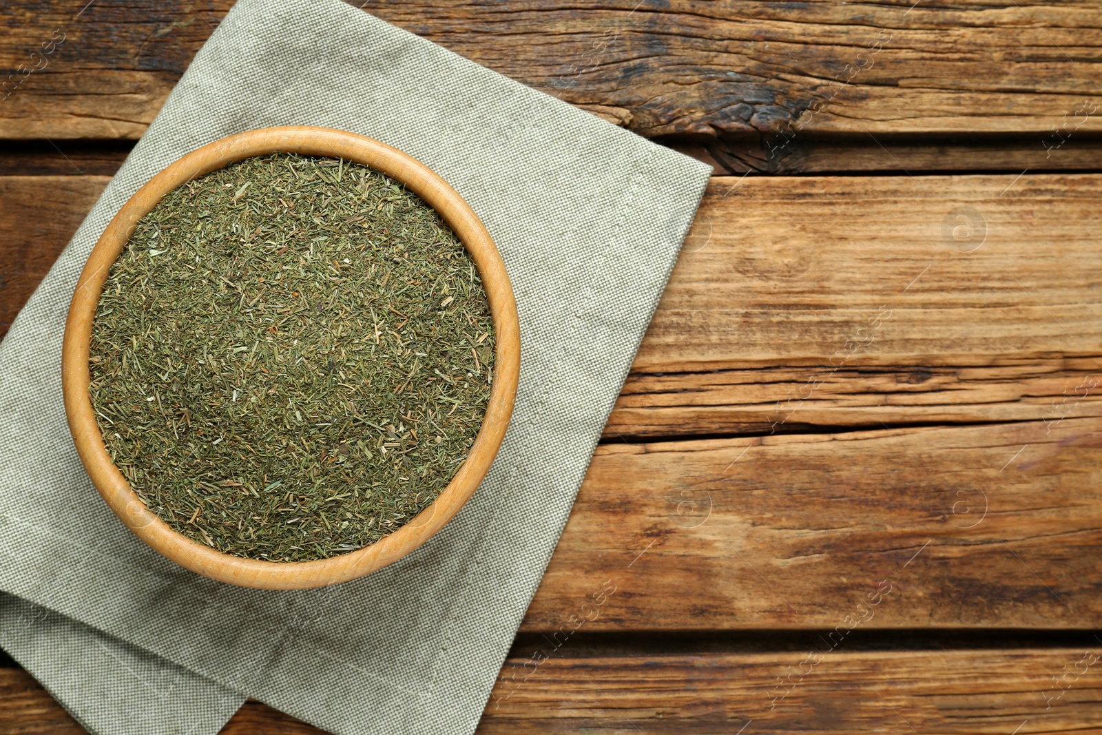 Photo of Bowl of dried dill on wooden table, top view. Space for text