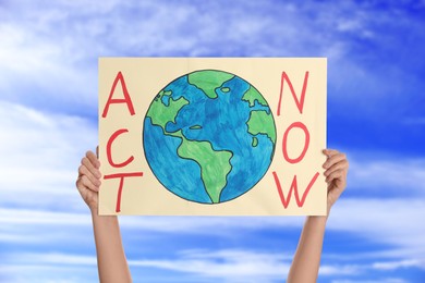 Image of Protestor holding placard with text Act Now against blue sky, closeup. Climate strike