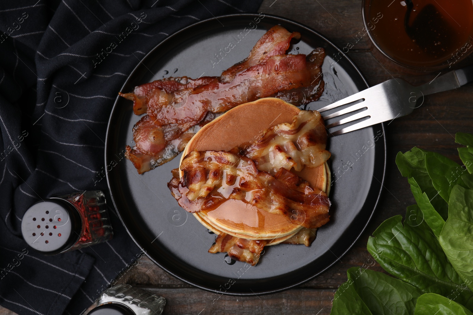 Photo of Delicious pancakes with fried bacon served on wooden table, flat lay