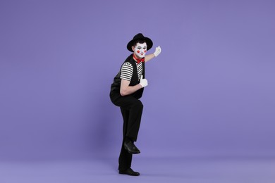 Funny mime artist in hat posing on purple background