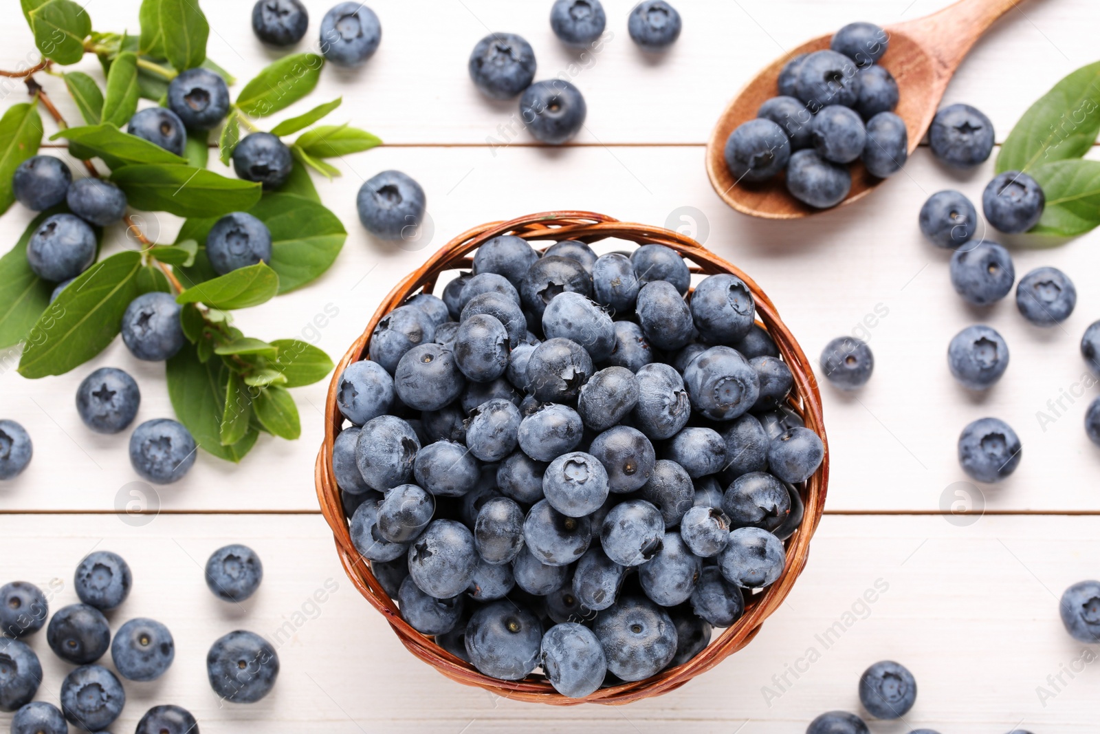 Photo of Tasty fresh blueberries and green leaves on white wooden table, flat lay