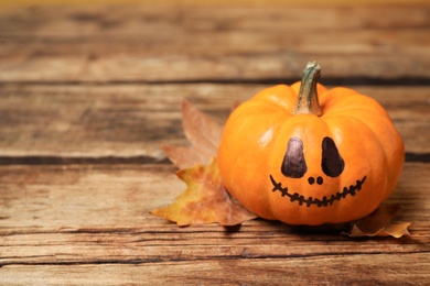 Photo of Pumpkin with scary face and fallen leaf on wooden background, space for text. Halloween decor