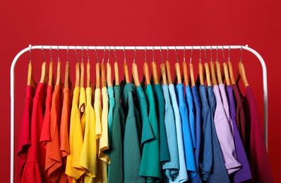 Photo of Rack with bright clothes on red background. Rainbow colors