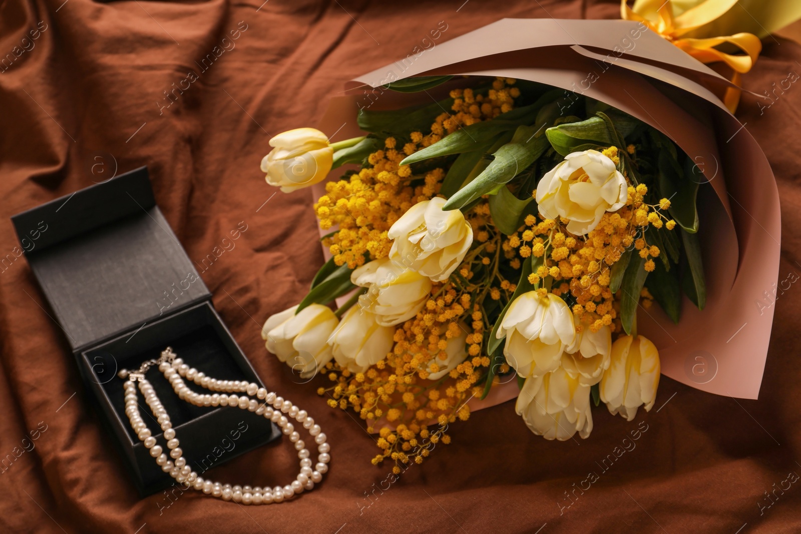 Photo of Bouquet of beautiful spring flowers and necklace on brown fabric, above view