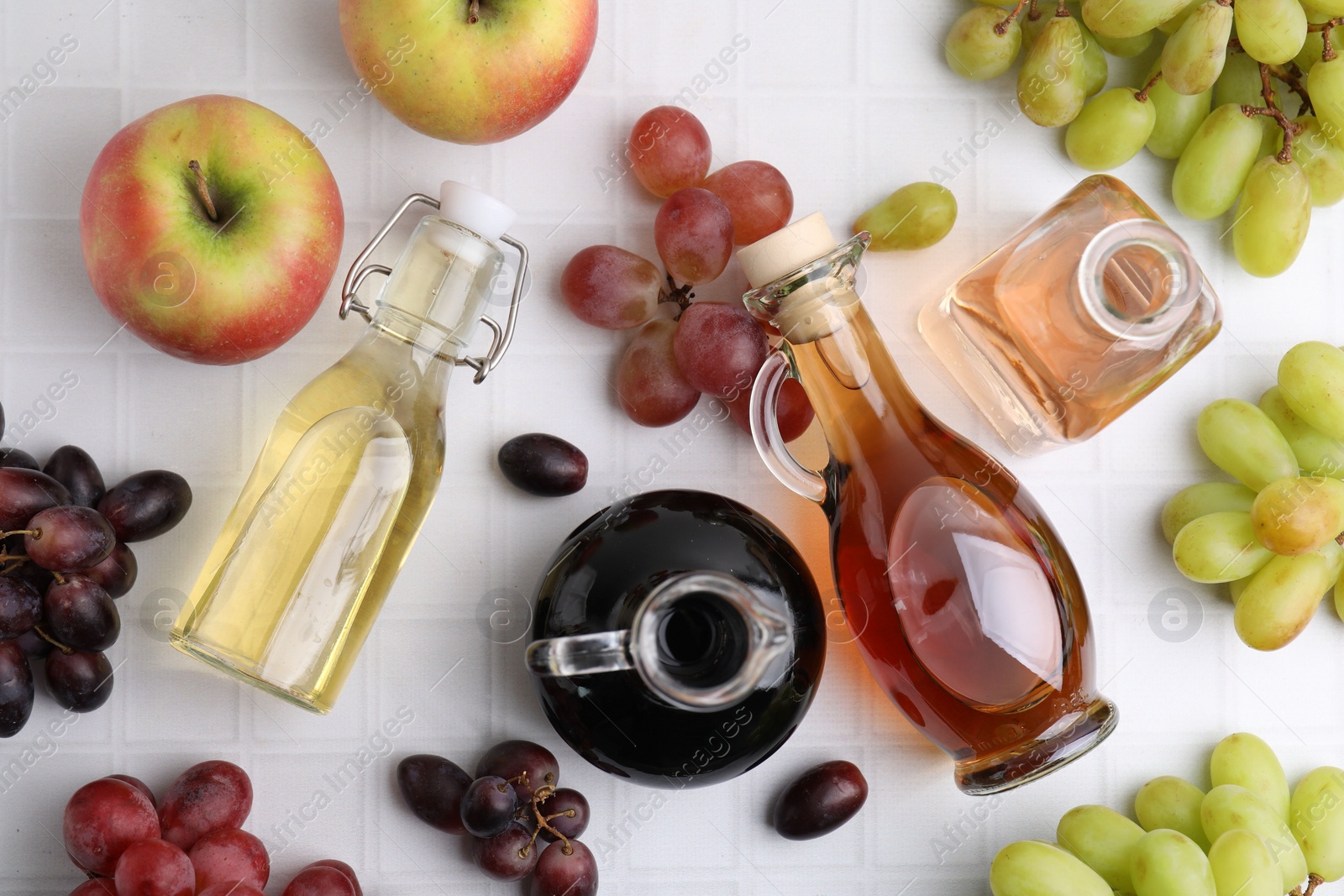 Photo of Different types of vinegar and ingredients on light tiled table, flat lay