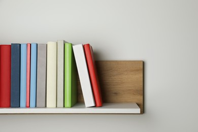 Many hardcover books on wooden shelf near white wall