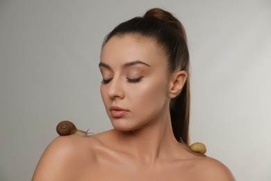 Photo of Beautiful young woman with snails on her body against grey background