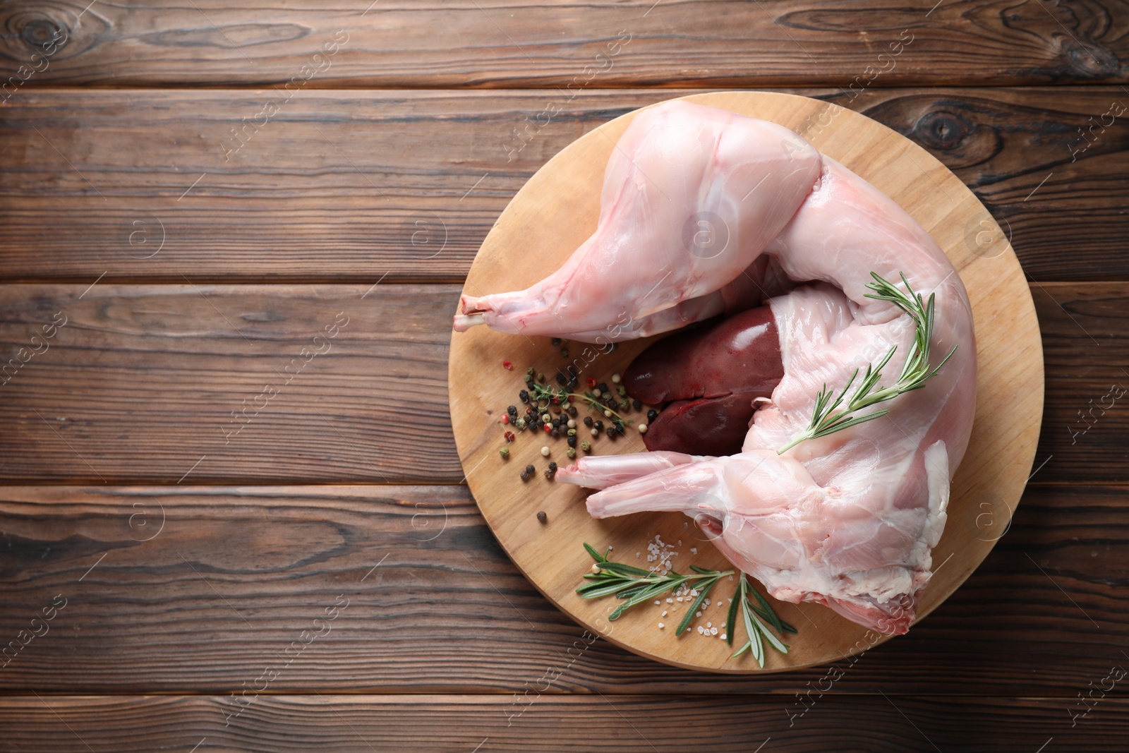 Photo of Whole raw rabbit, liver and spices on wooden table, top view. Space for text