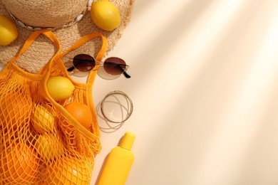 Photo of String bag with sunglasses, fruits and summer accessories on beige background, flat lay. Space for text