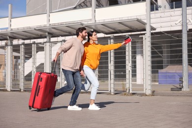 Being late. Couple with red suitcase running outdoors, space for text