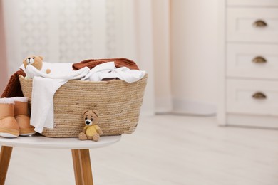 Photo of Laundry basket with baby clothes, shoes and crochet toys on white wooden table in child room, space for text