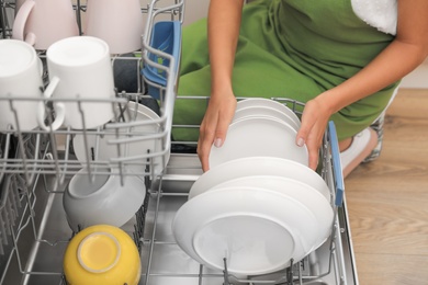 Young woman loading dishwasher in kitchen, closeup. Cleaning chores