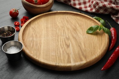 Photo of Cutting board, salt, spices, basil and chili peppers on black textured table. Space for text