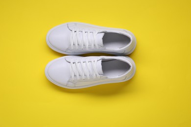 Photo of Pair of stylish white sneakers on yellow background, top view