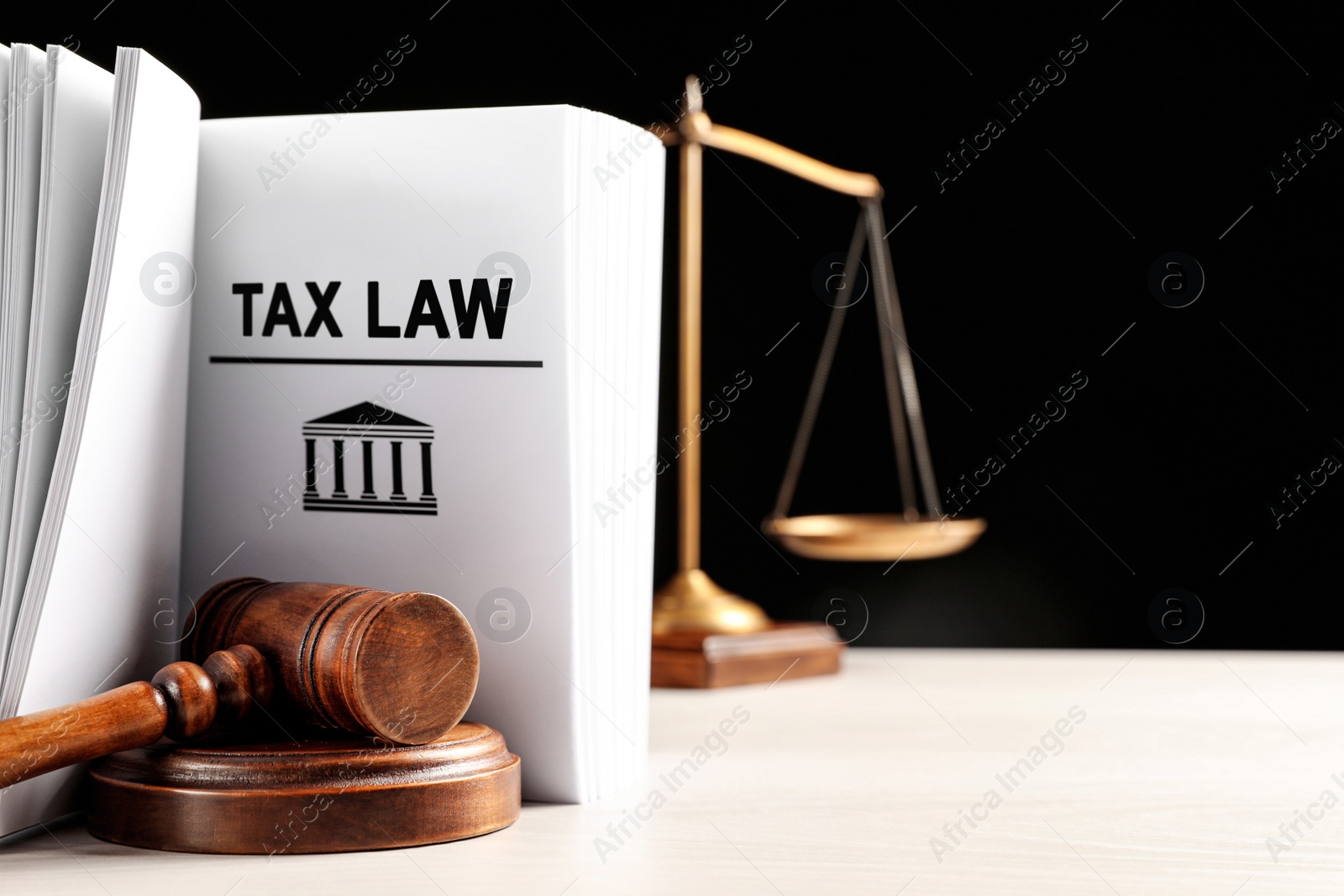 Image of Tax law book, judge's gavel and scales on white table against black background. Space for text