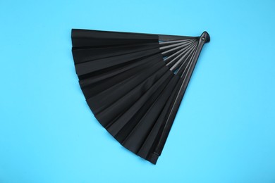 Stylish black hand fan on light blue background, top view