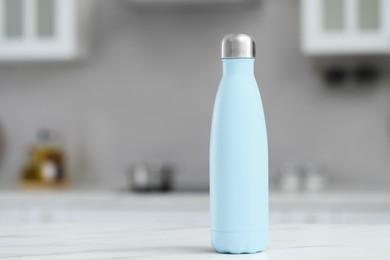 Stylish thermo bottle on white table in kitchen. Space for text