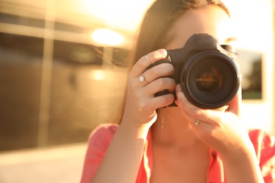 Photo of Young photographer taking picture with professional camera outdoors, closeup