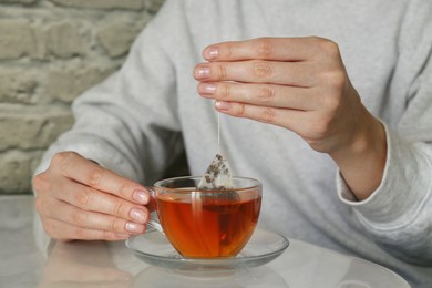 Woman taking tea bag out of cup at table indoors, closeup