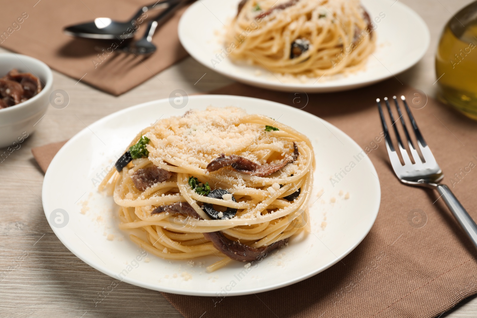 Photo of Plates of delicious pasta with anchovies, olives and parmesan cheese served on light wooden table