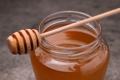 Photo of Sweet golden honey in jar and dipper on grey table, closeup