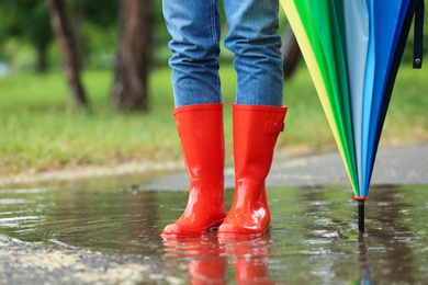 Photo of Woman with umbrella and rubber boots in puddle, closeup. Rainy weather