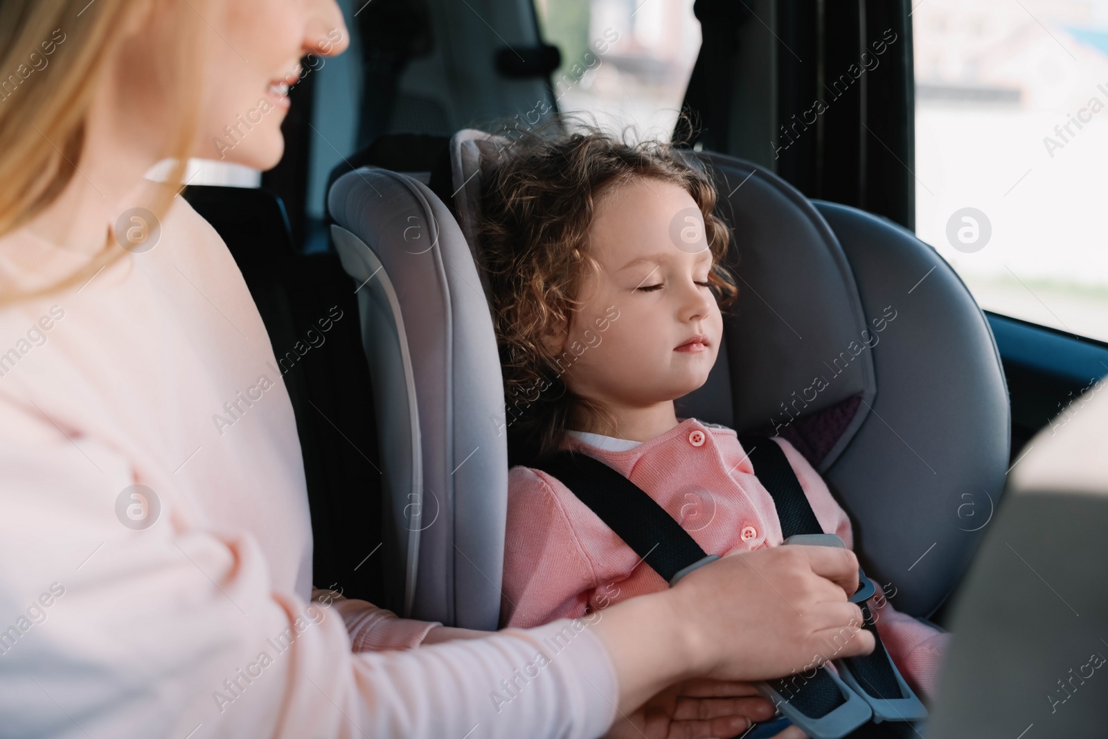 Photo of Mother fastening her daughter in child safety seat inside car