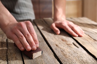 Photo of Man polishing wooden table with sandpaper indoors, closeup