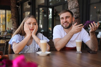 Photo of Young woman having boring date with talkative guy in outdoor cafe