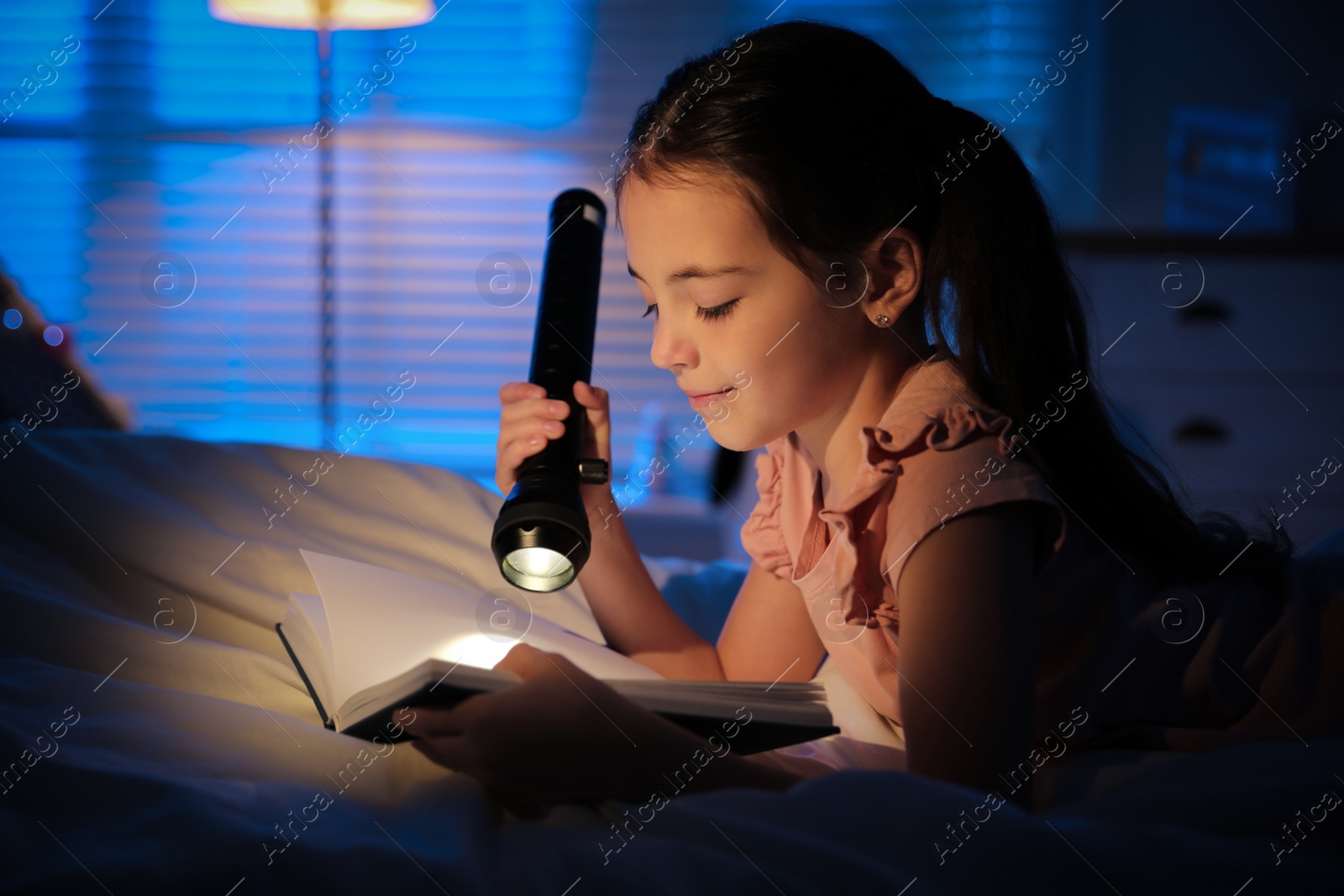 Photo of Little girl with flashlight reading fairy tale in dark bedroom