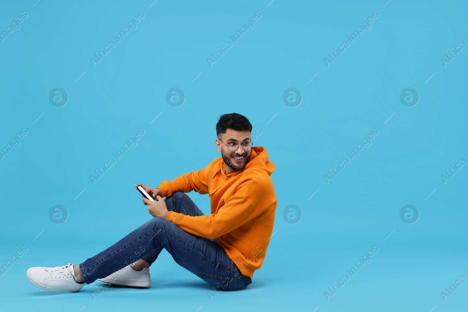 Photo of Happy young man using smartphone on light blue background, space for text