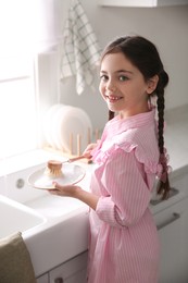 Photo of Little girl washing dishes in kitchen at home