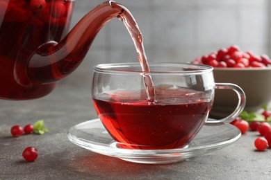 Photo of Pouring hot cranberry tea into glass cup and fresh berries on light grey textured table, closeup