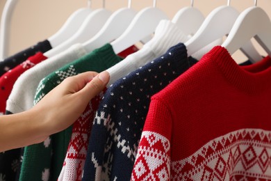 Woman choosing Christmas sweater from rack, closeup